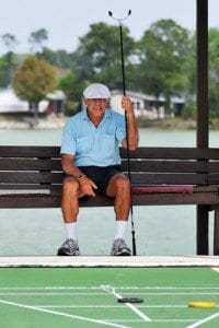 Senior man sitting on a bench with cue in hand, waiting for his turn at shuffleboard.